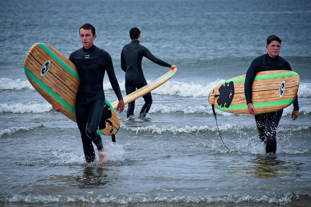 2 men in black wet suit holding green and yellow surfboard on sea during daytime