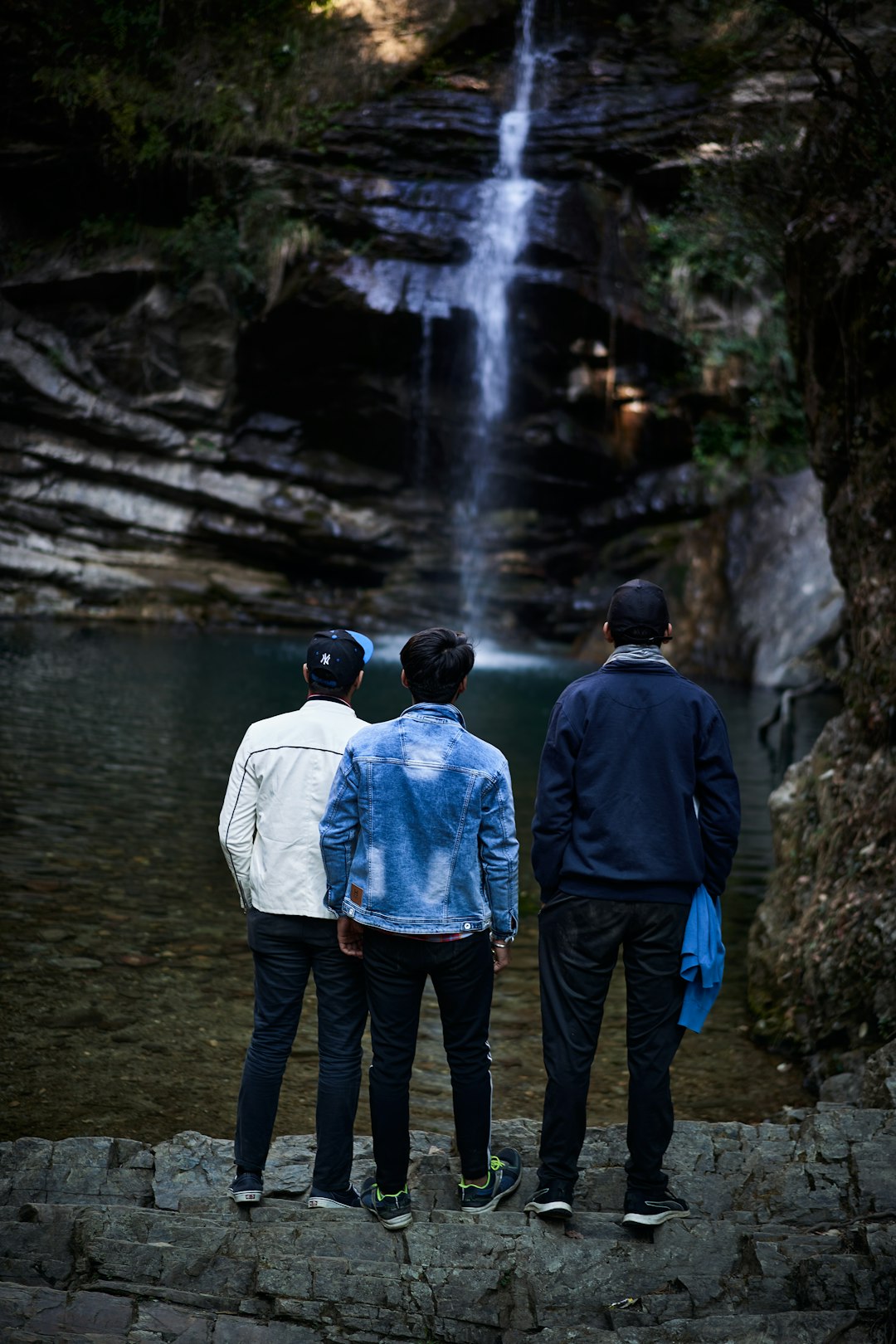 man in blue jacket standing beside man in blue jacket near waterfalls during daytime