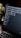 A close-up view of a laptop screen displaying a project management tool with columns labeled 'Open', 'In Progress', and 'Review'. Tasks are listed under each column. The environment appears dimly lit, with a small, leafy plant visible in the background.