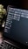 A close-up view of a laptop screen displaying a project management tool with columns labeled 'Open', 'In Progress', and 'Review'. Tasks are listed under each column. The environment appears dimly lit, with a small, leafy plant visible in the background.