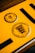 A close-up of a yellow vehicle registration plate displaying black symbols and text. The upper section features a circular inspection sticker with numerical markings from 1 to 12 and a highlighted number 10 in the center. Below, a circular emblem contains the text 'Baden-Württemberg' and a stylized coat of arms with lions.