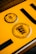 A close-up of a yellow vehicle registration plate displaying black symbols and text. The upper section features a circular inspection sticker with numerical markings from 1 to 12 and a highlighted number 10 in the center. Below, a circular emblem contains the text 'Baden-Württemberg' and a stylized coat of arms with lions.