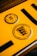 A close-up of a yellow vehicle registration plate displaying black symbols and text. The upper section features a circular inspection sticker with numerical markings from 1 to 12 and a highlighted number 10 in the center. Below, a circular emblem contains the text 'Baden-Württemberg' and a stylized coat of arms with lions.