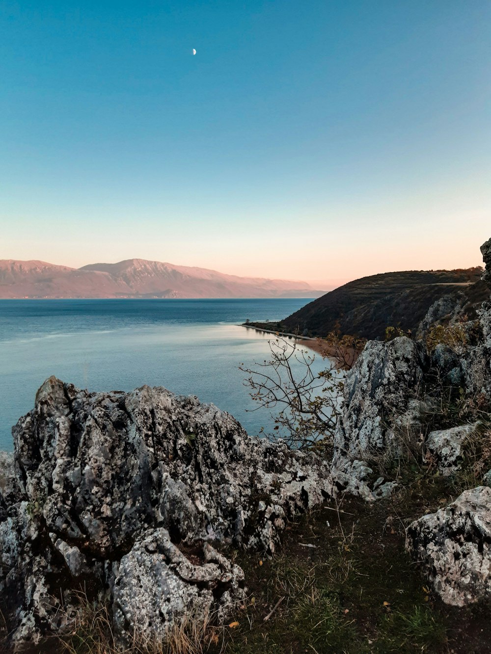 brown and green mountain beside blue sea under blue sky during daytime