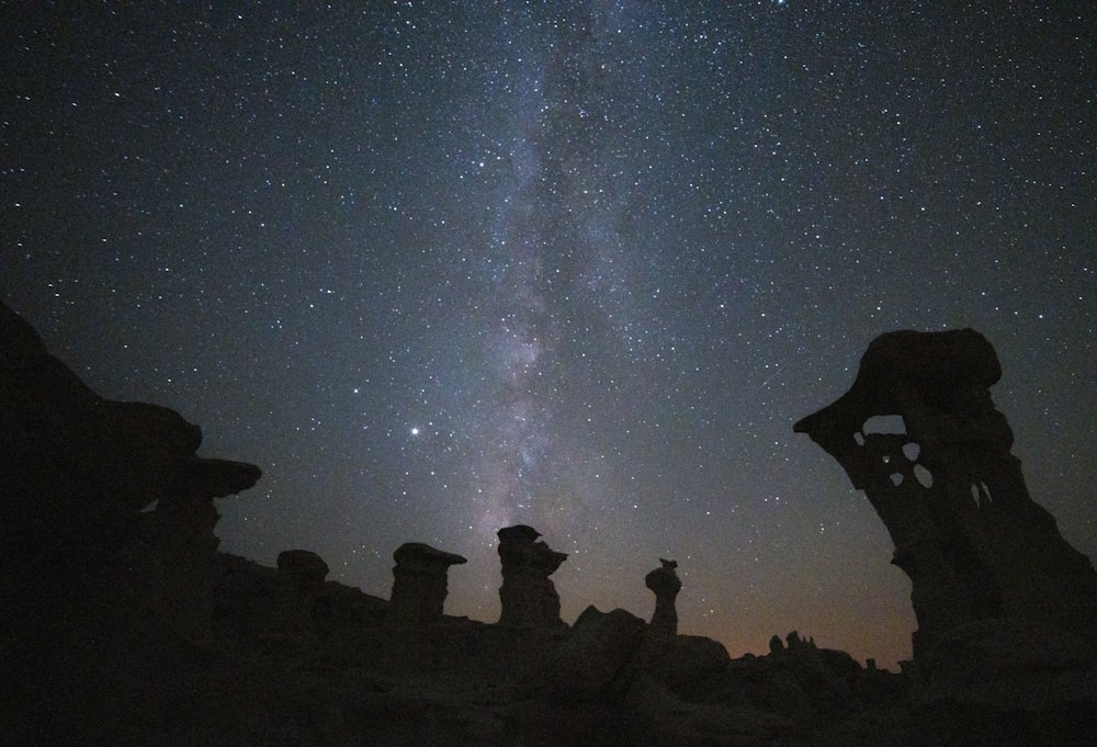 silhouette de personnes sur la formation rocheuse sous la nuit étoilée