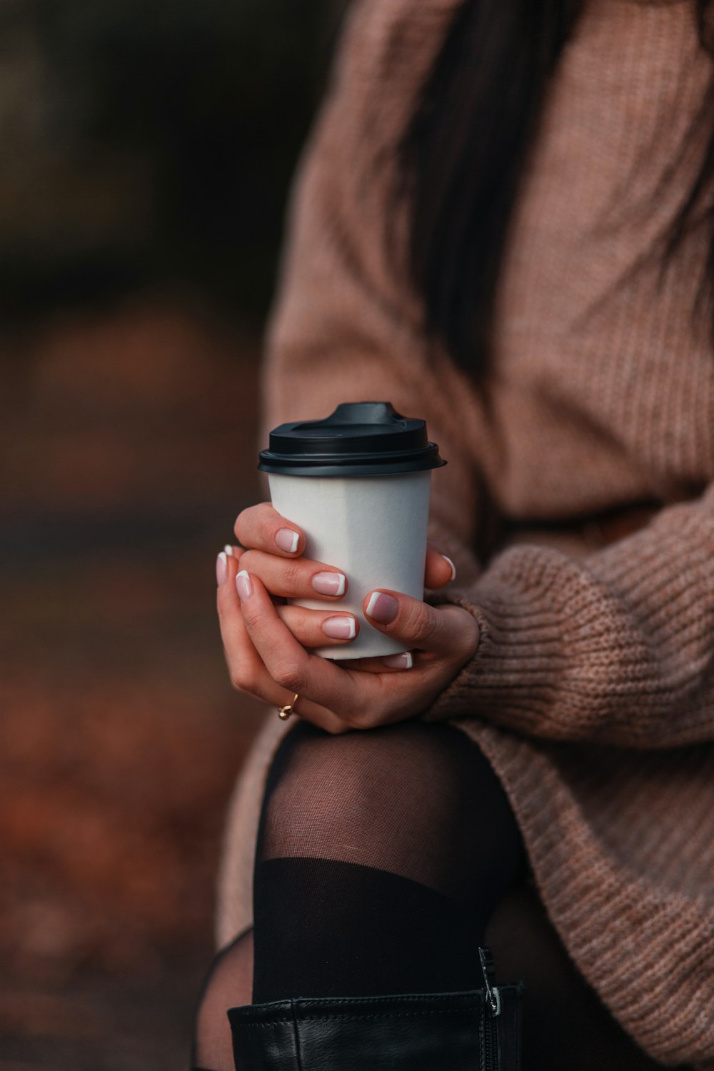 woman in brown sweater holding white disposable cup