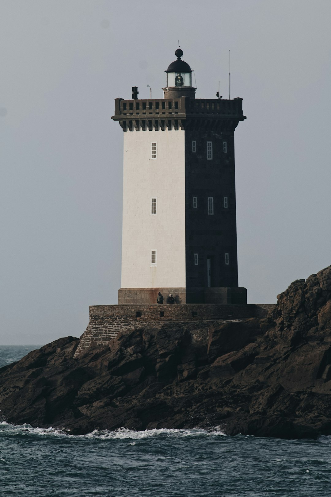 white and brown lighthouse on brown rock formation near body of water during daytime