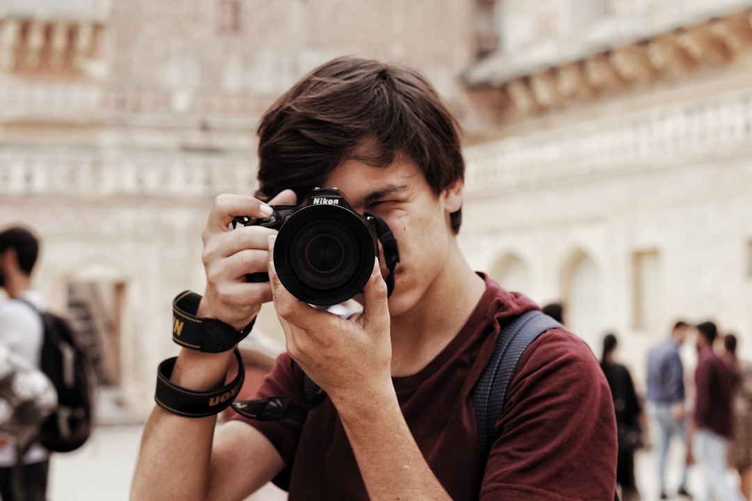 man in red and black crew neck t-shirt holding black nikon dslr camera