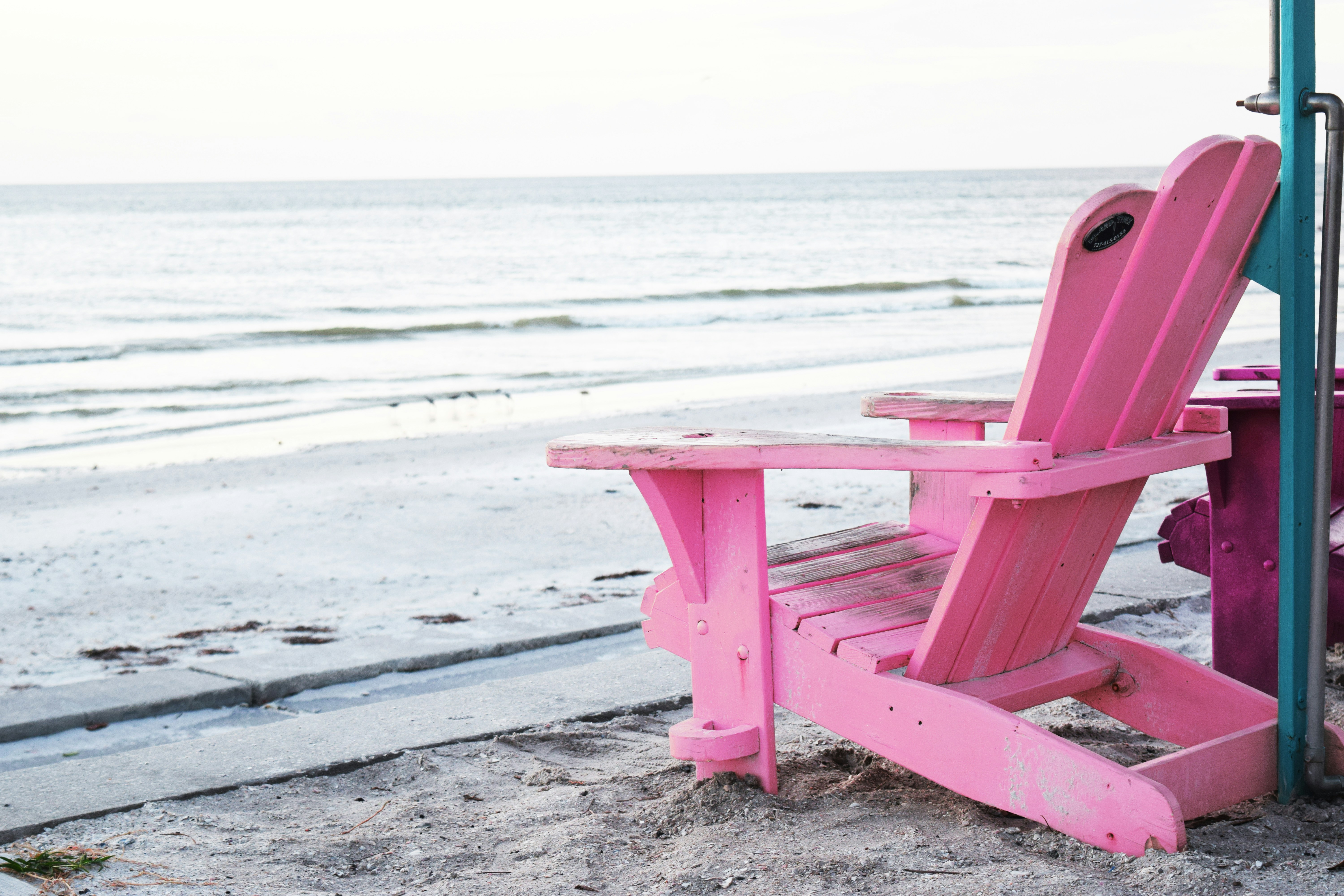 red wooden chair on beach during daytime, pink chair on the beach