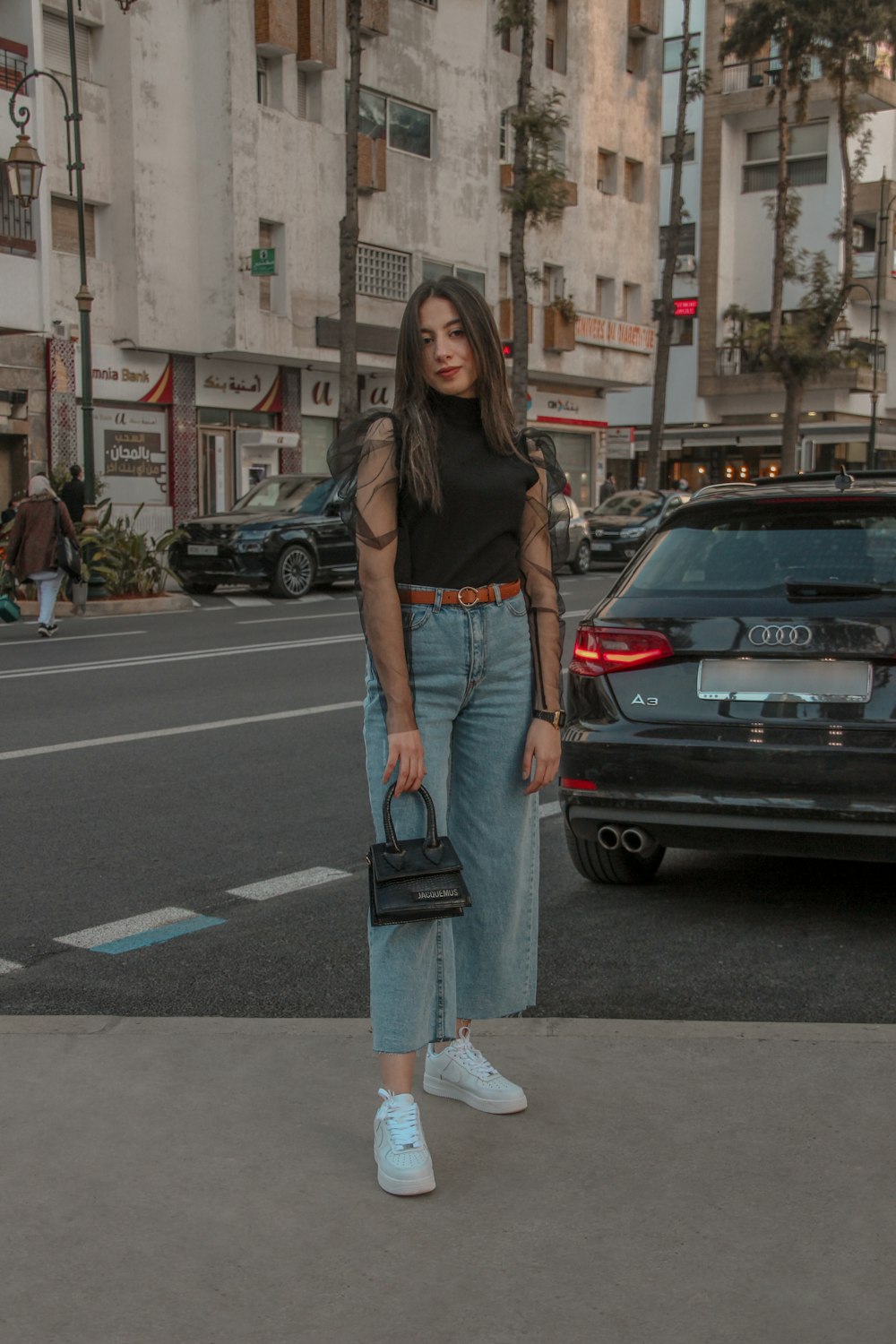 woman in black shirt and blue denim jeans standing on sidewalk during daytime