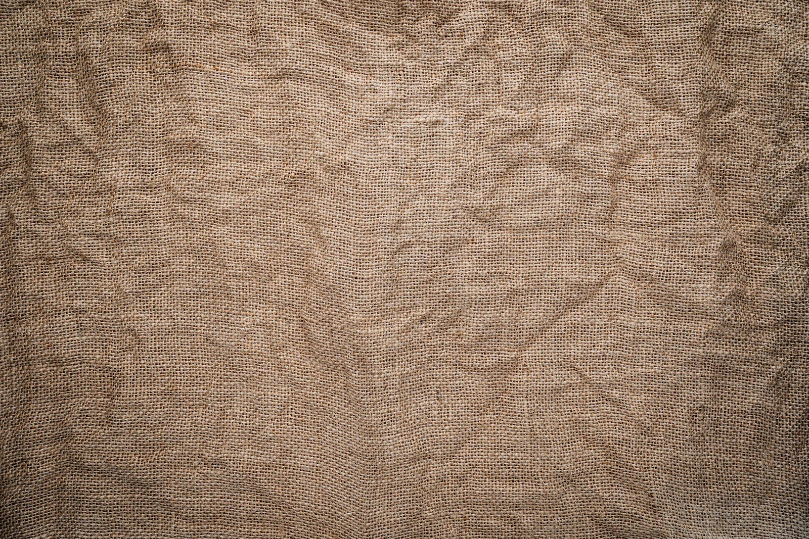 Coarse undyed cloth in a warm earth tone, laid on bare wood.
