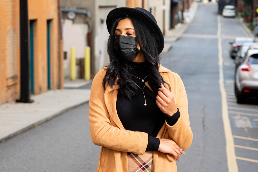 woman in black long sleeve shirt and brown coat standing on sidewalk during daytime