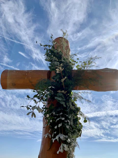 Children joyfully singing hymns around a wooden cross outdoors.