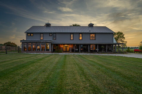 A sleek luxury barndominium with warm wood accents and metal siding under a bright blue sky.