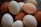 A collection of eggs in various colors, predominantly brown, cream, and pale blue, stacked together in a bowl or similar container. The eggs are closely packed, showcasing their smooth, unblemished surfaces.