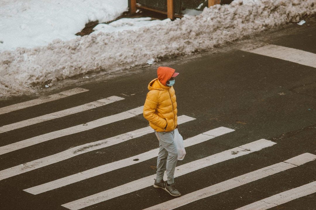 person in yellow jacket and white pants walking on pedestrian lane during daytime