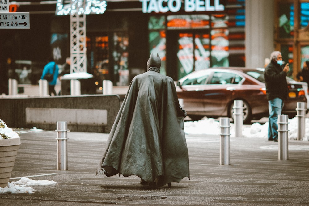 person in gray robe sitting on sidewalk during daytime