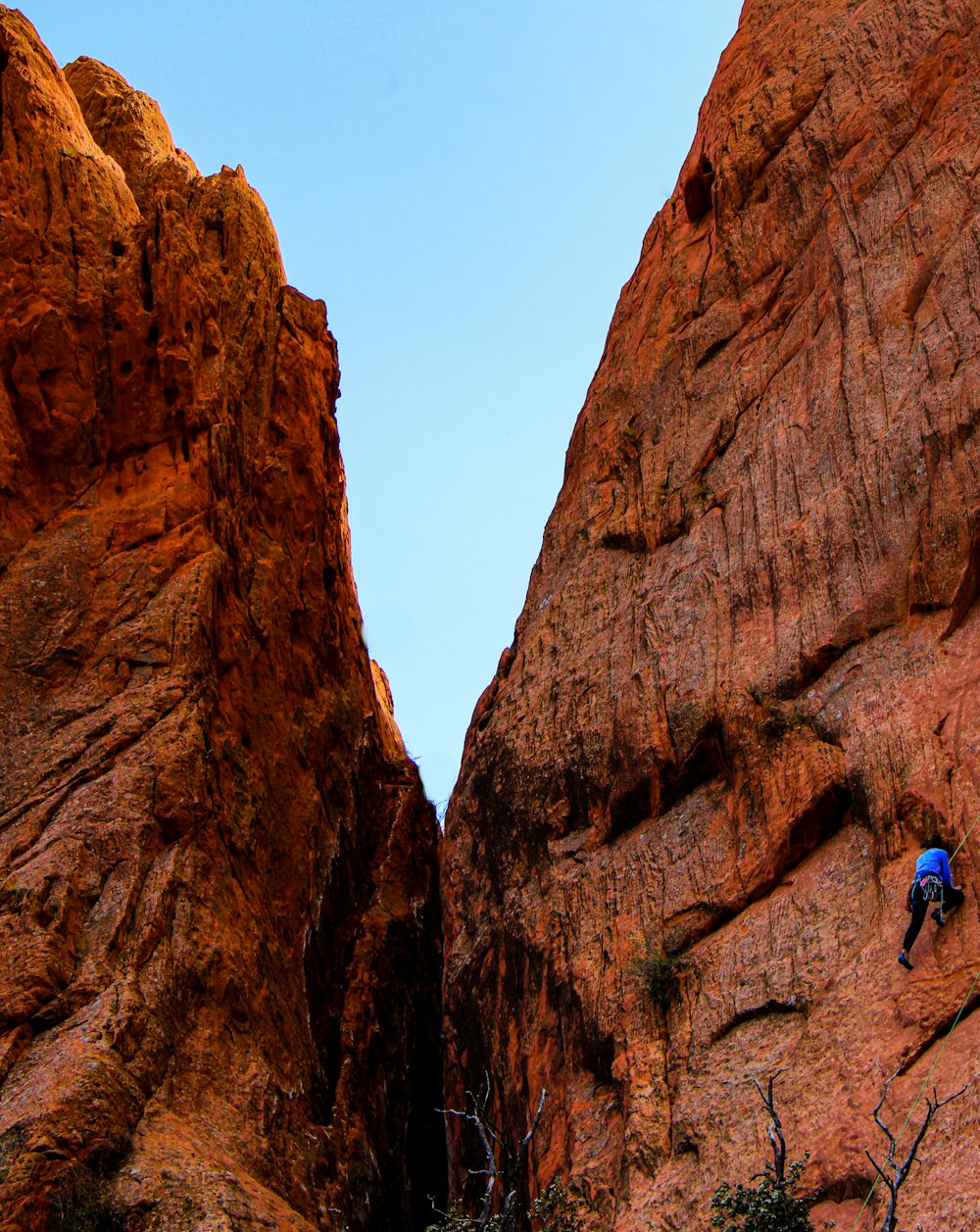 man in blue shirt climbing brown rock mountain during daytime