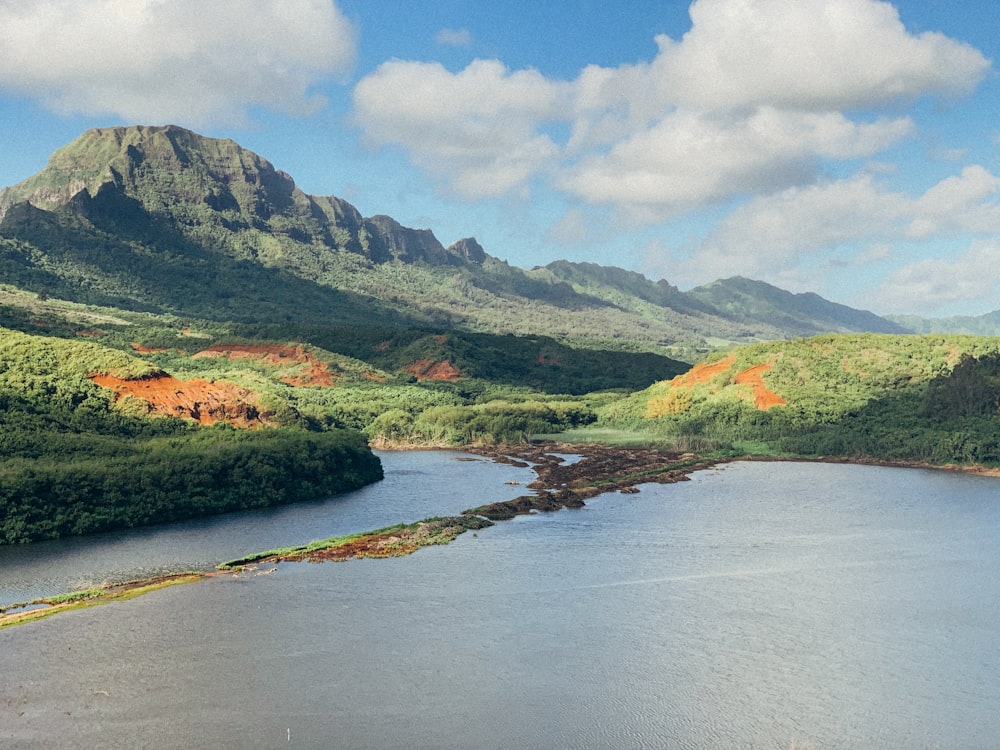 green mountains beside river under white clouds and blue sky during daytime