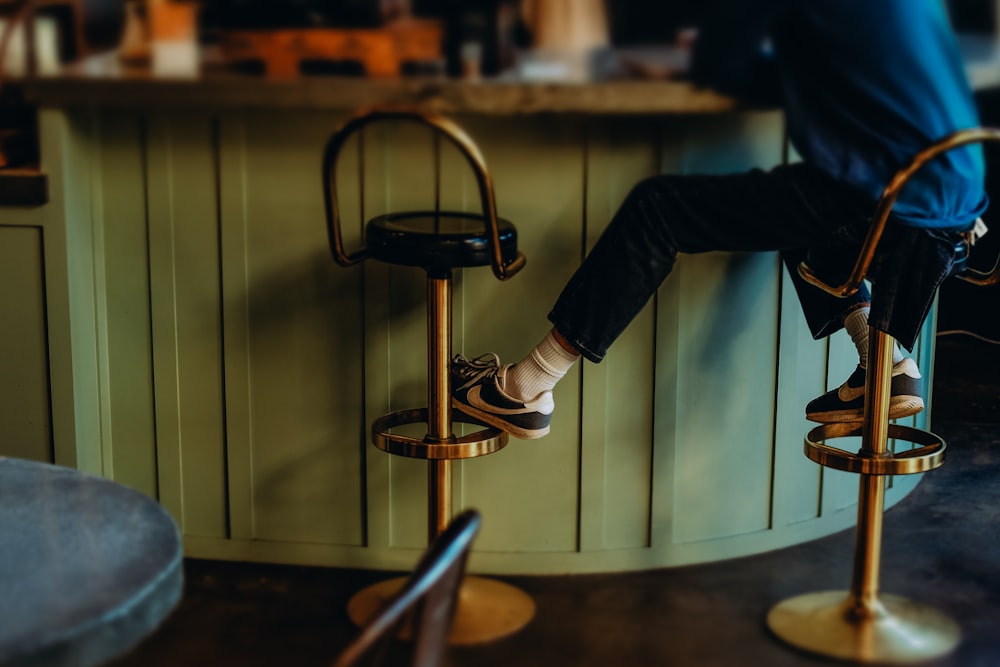 person in black pants and black and white sneakers sitting on bar seat