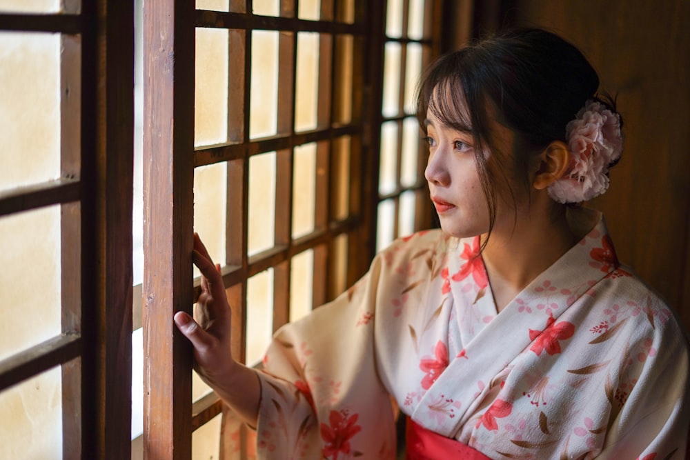 woman in white and red floral robe standing beside brown wooden window