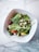 A fresh salad in a square white bowl on a marble surface, containing spinach leaves, grape tomatoes, crumbled feta cheese, black olives, and yellow bell pepper pieces.