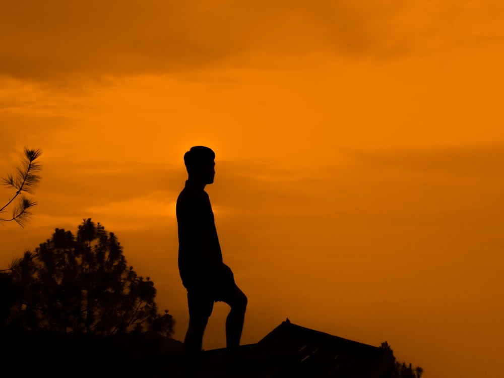 Silueta del hombre de pie sobre la roca durante la puesta del sol
