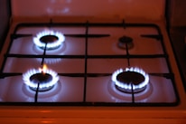 Four gas stove burners are visible, with three of them lit and displaying blue flames. The stove has a metal grate over the burners and a white surface.