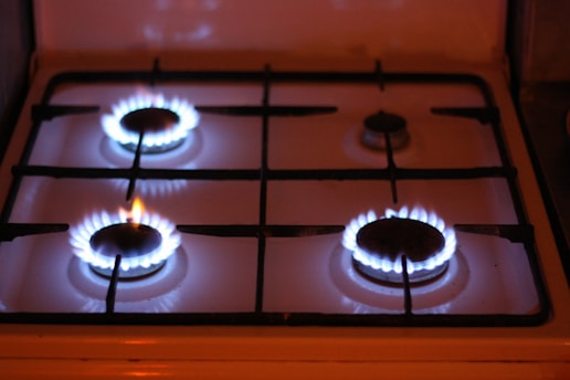Four gas stove burners are visible, with three of them lit and displaying blue flames. The stove has a metal grate over the burners and a white surface.