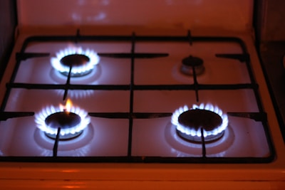 Four gas stove burners are visible, with three of them lit and displaying blue flames. The stove has a metal grate over the burners and a white surface.