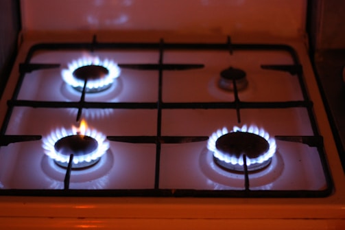 Four gas stove burners are visible, with three of them lit and displaying blue flames. The stove has a metal grate over the burners and a white surface.