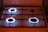 Four gas stove burners are visible, with three of them lit and displaying blue flames. The stove has a metal grate over the burners and a white surface.