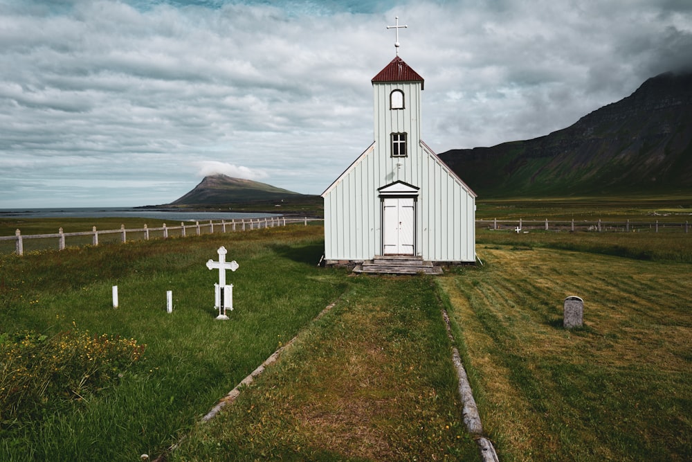 weiße Holzkirche auf grünem Grasfeld unter weißen Wolken und blauem Himmel tagsüber