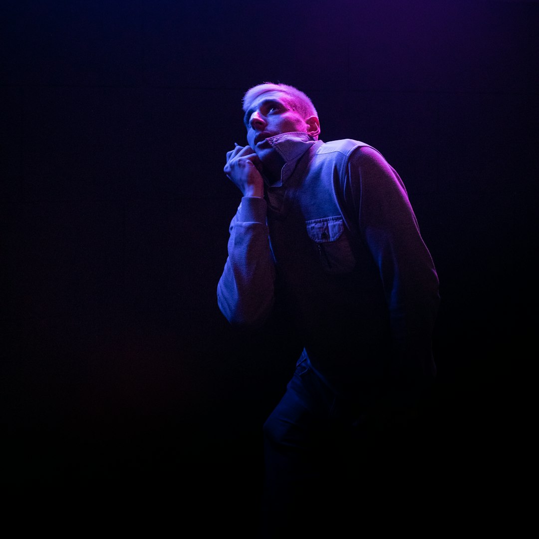 man in black jacket and blue denim jeans holding microphone