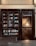 A storefront with glass windows displaying books on shelves. The book covers are of various colors and designs. There is a glass door on the right side, illuminated by warm light from inside, revealing a staircase.