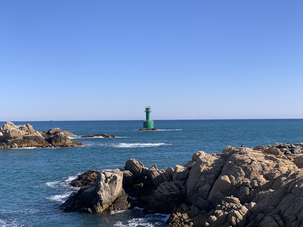green lighthouse on rocky shore during daytime