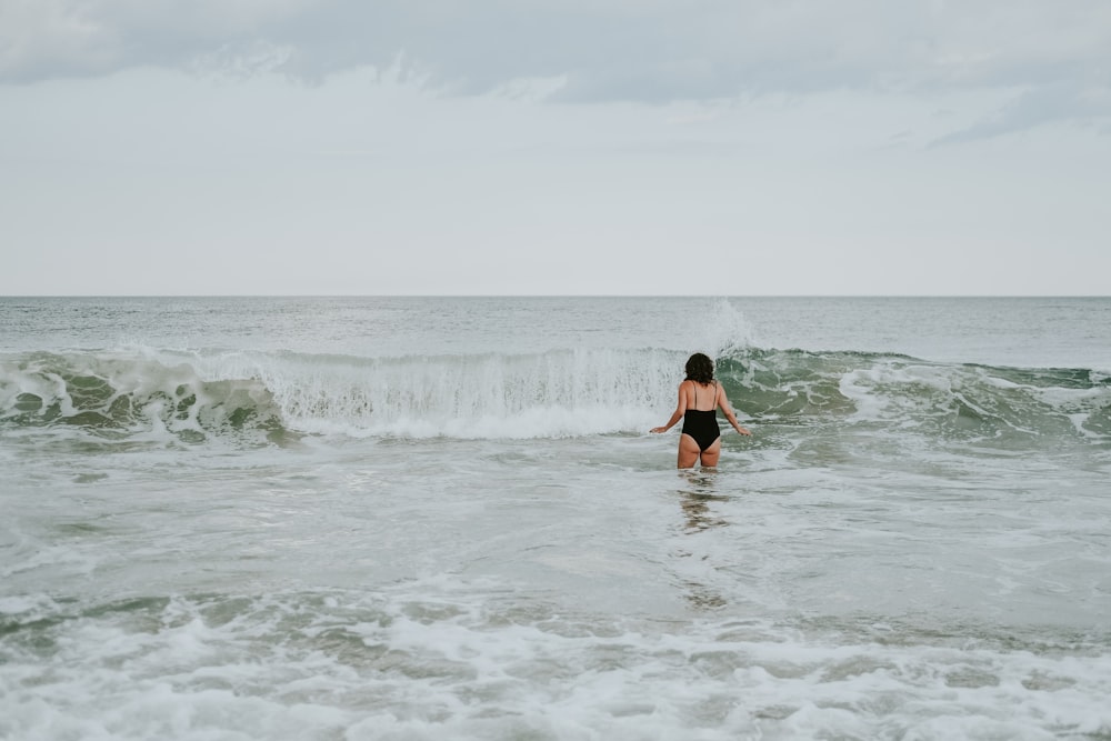 woman in black bikini walking on sea waves during daytime