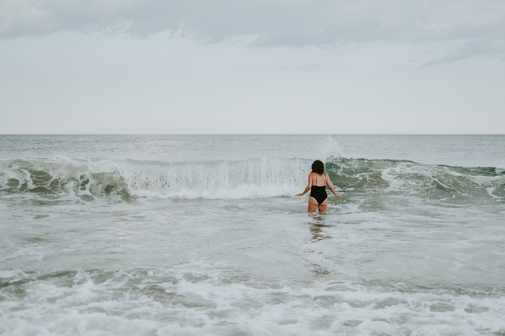 昼間、海の波の上を歩く黒いビキニの女性