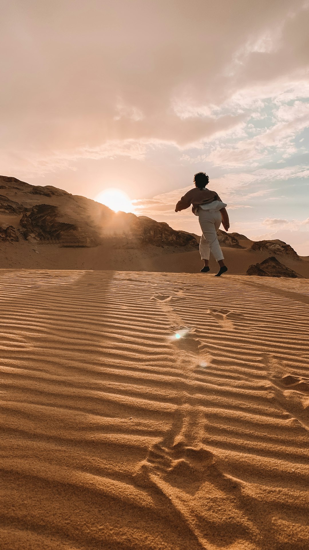 man in black jacket and white pants walking on sand during daytime