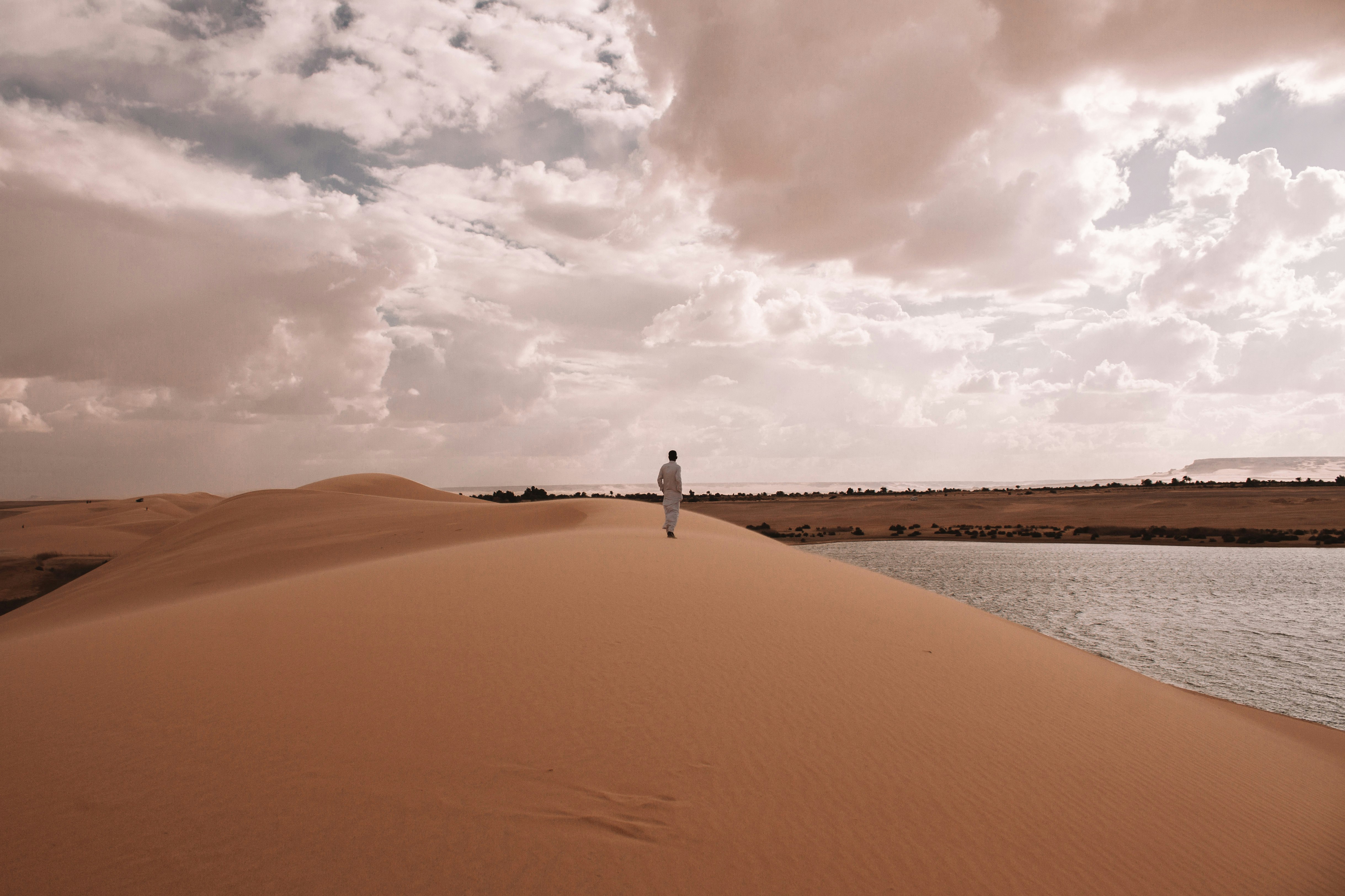person standing on brown sand under white clouds during daytime