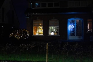 A warmly lit home exterior at dusk, decorated with festive holiday lights along the roofline and gutters.