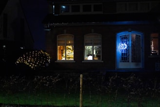 A warmly lit Christmas wreath hangs on a door, glowing softly with red, white, and gold lights.