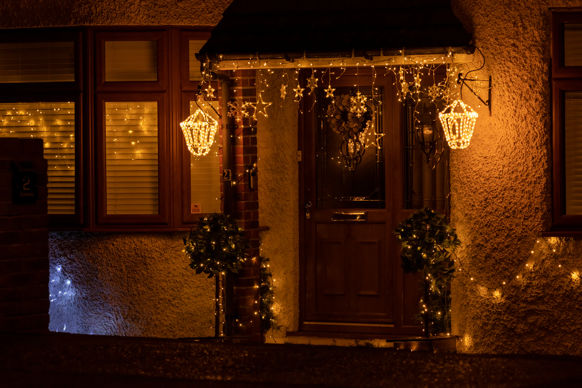 Home entry with lit lanterns, garland and warm lights framing the front door at night