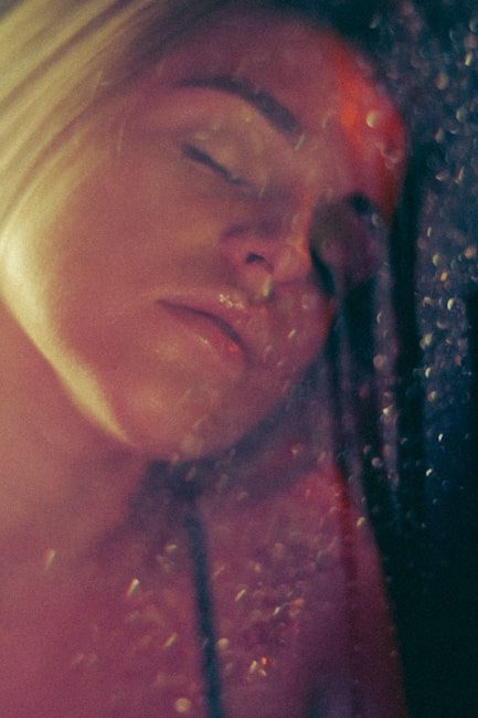 A close-up, soft-focused image of a person's face with eyes closed, illuminated by gentle light, creating a dreamy and serene atmosphere. The image includes scattered light reflections and a warm color palette.