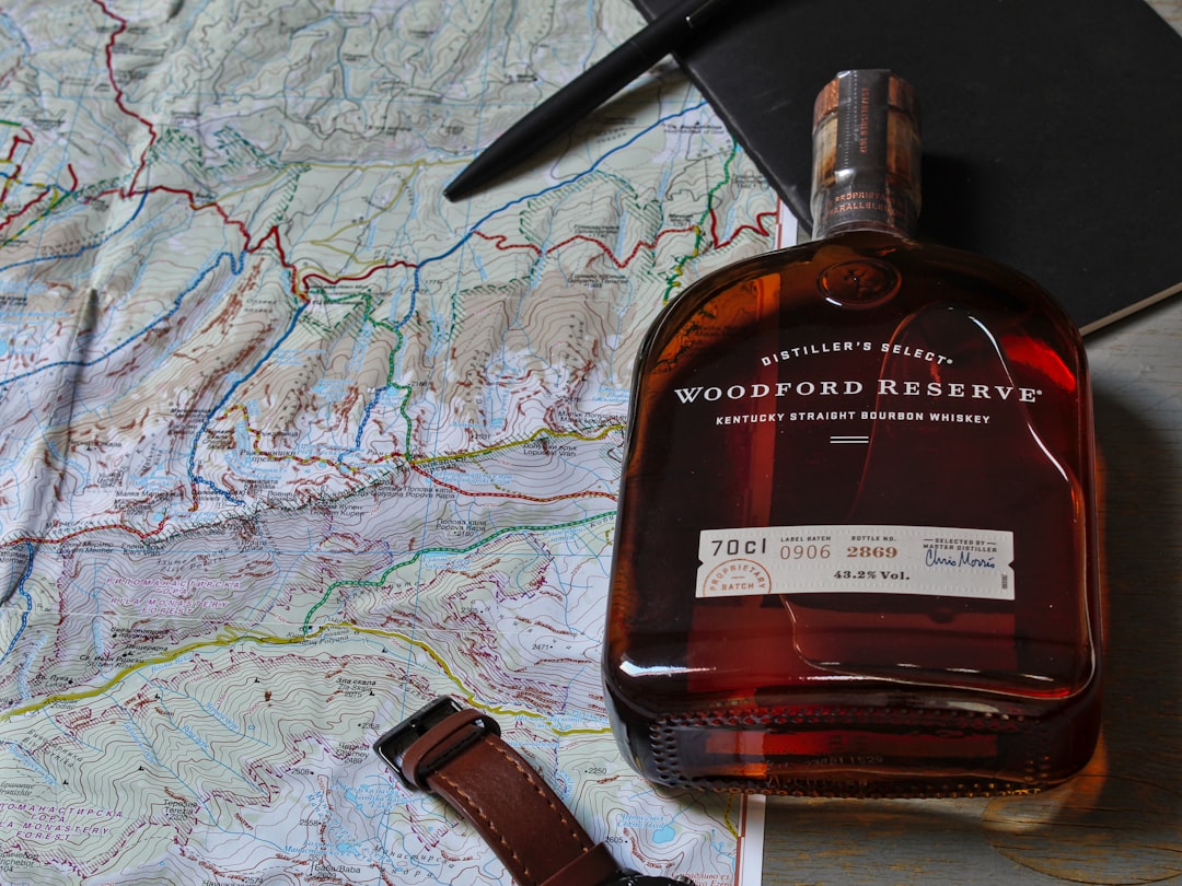black handle knife beside brown glass bottle, A bottle of whiskey next to a map.