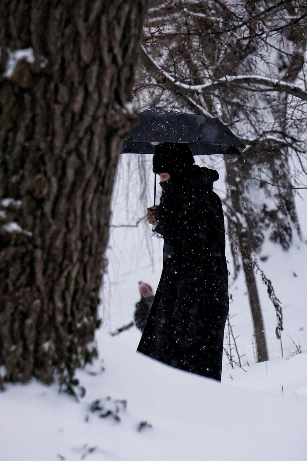 woman in black dress holding umbrella standing on snow covered ground during daytime