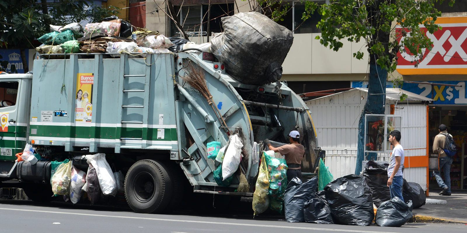 Worker standing beside a green collection truck on a residential street
