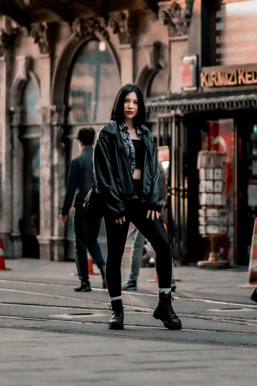 man in black leather jacket and black pants standing on sidewalk during daytime