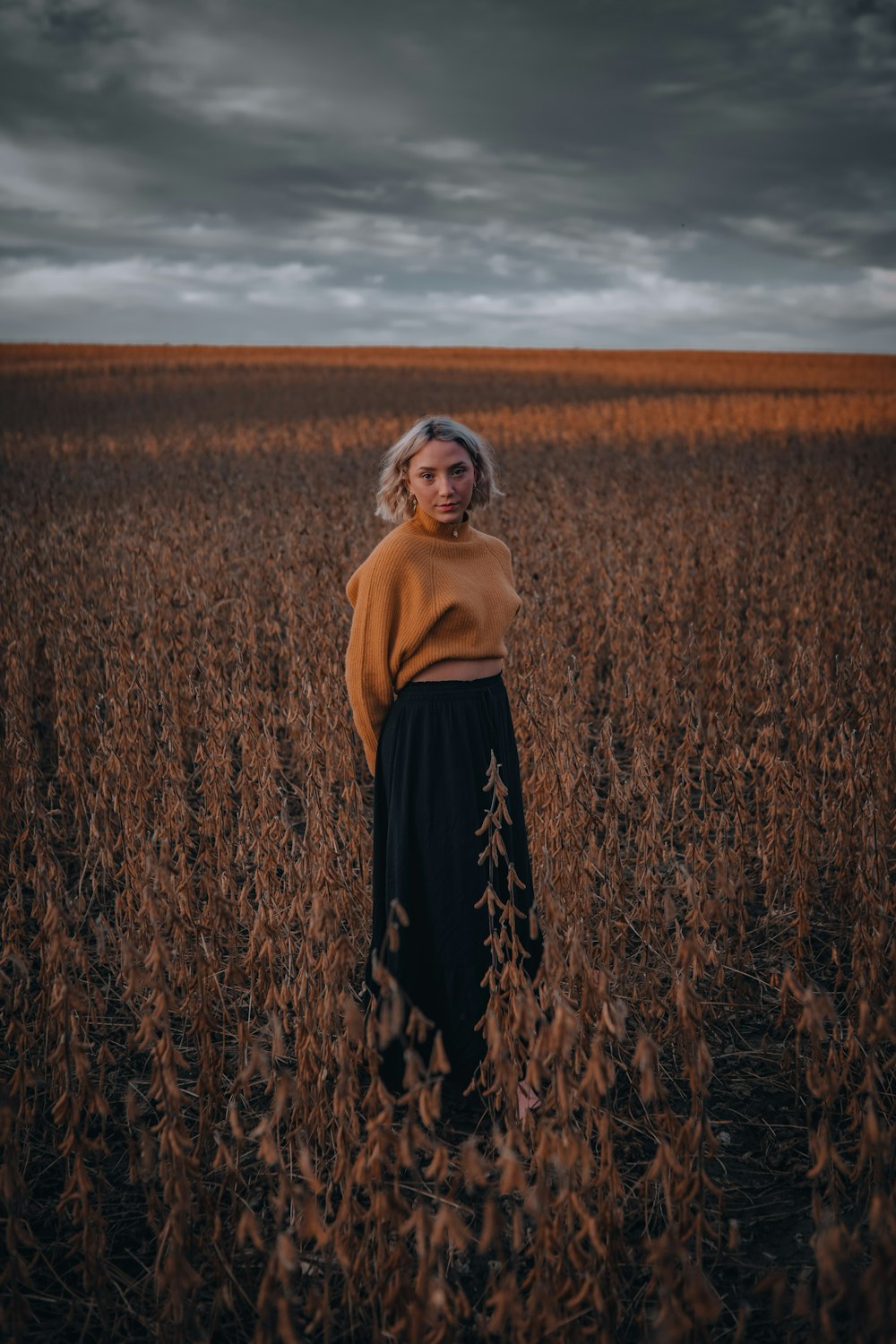 woman in brown long sleeve shirt and black skirt standing on brown grass field during daytime