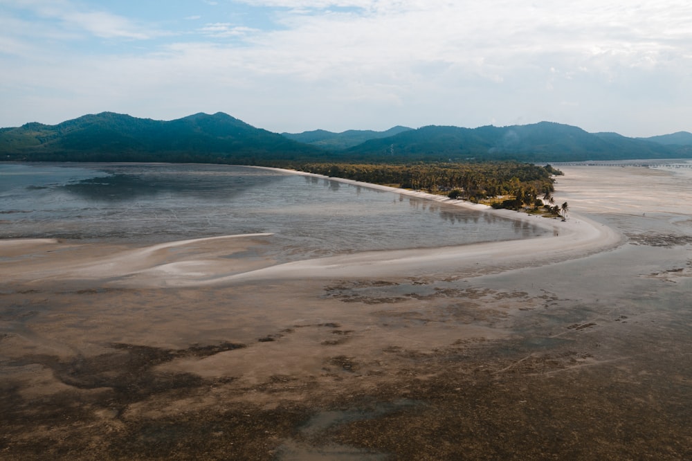 body of water near mountain under white clouds during daytime